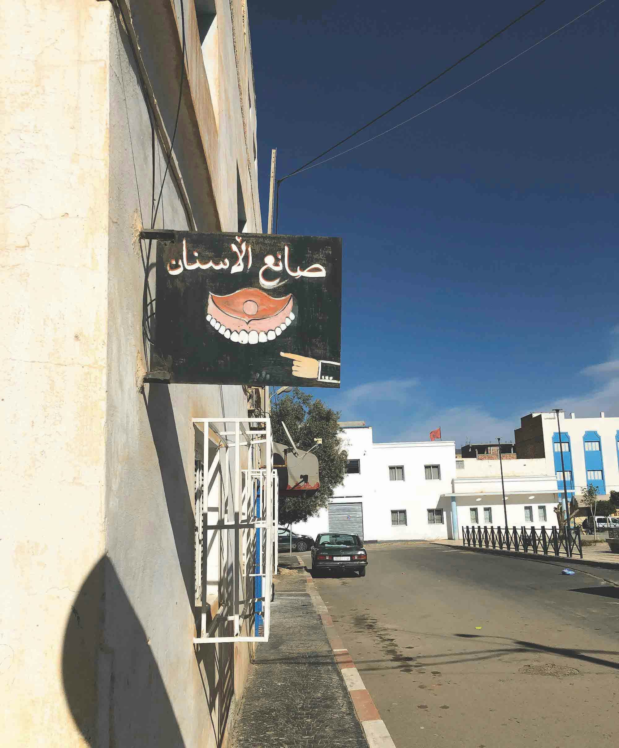 Image of a Moroccan street with a illustrated sign of a dentist. © MAryam Touzani