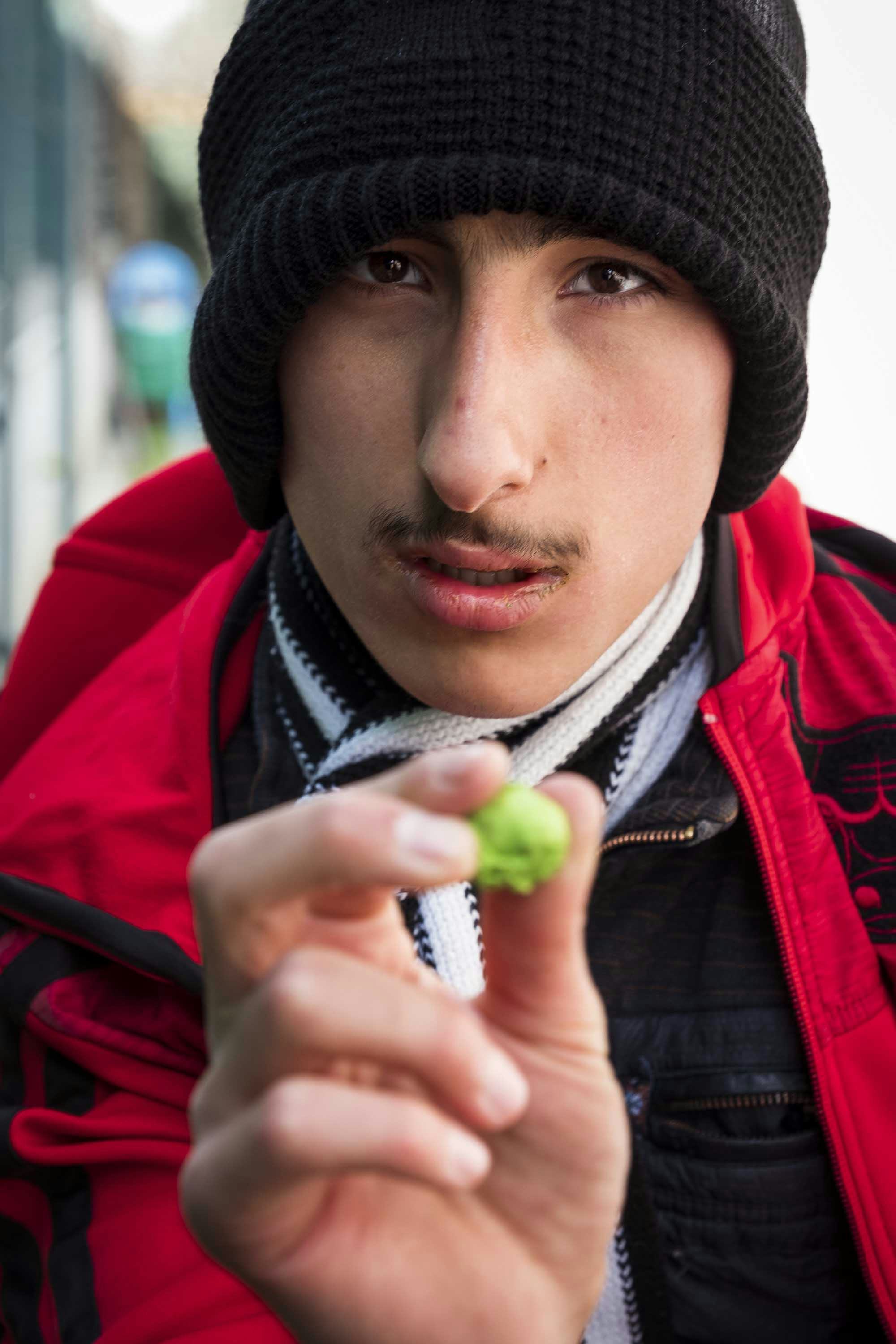 Portrait of a boy wearing a red jacket, holding up a small green token. © Oğulcan Arslan