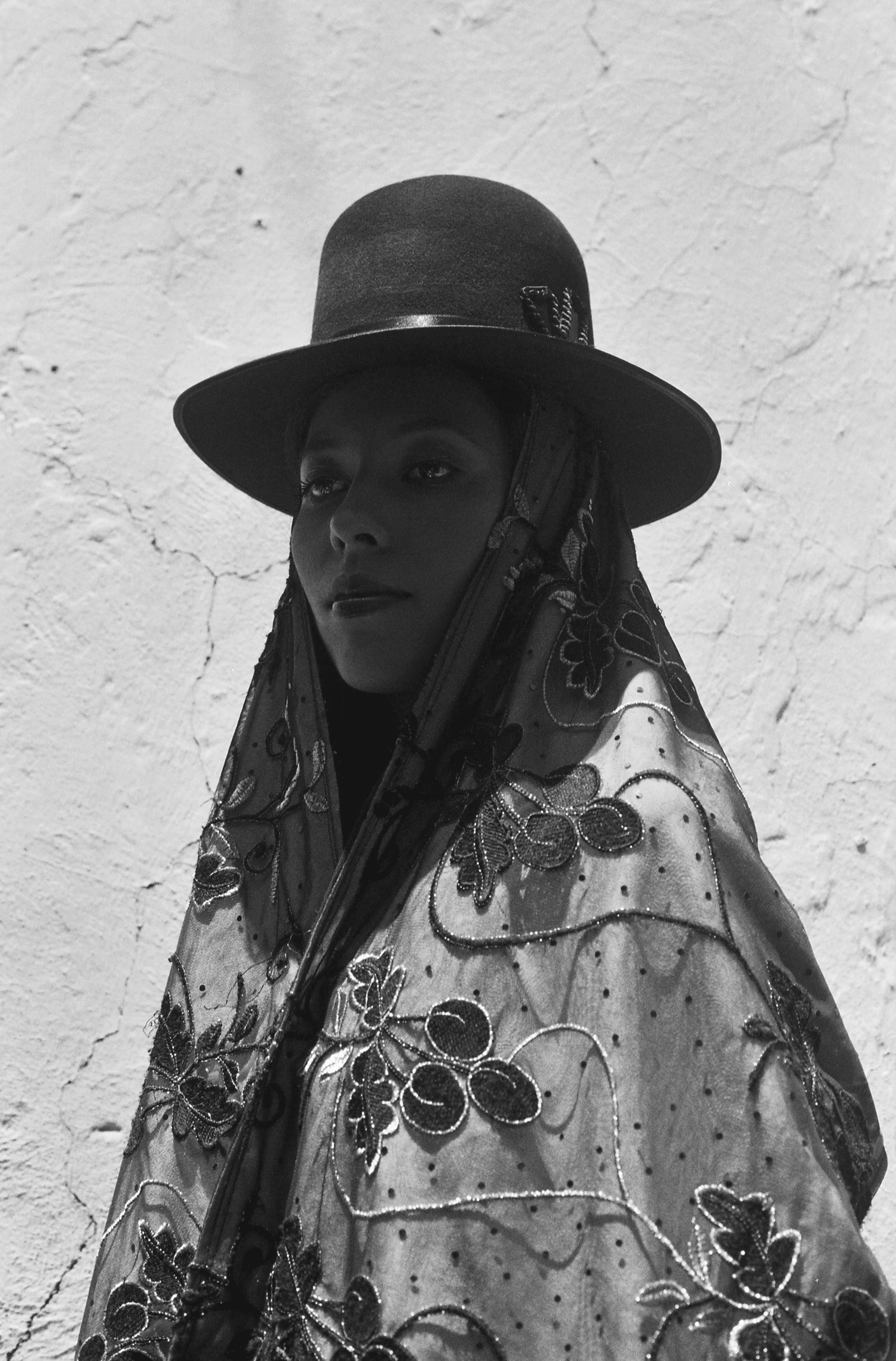 Black and white portrait of a Bolivian woman wearing an embroidered cloth around her shoulders and hat. © Marisol Mendez