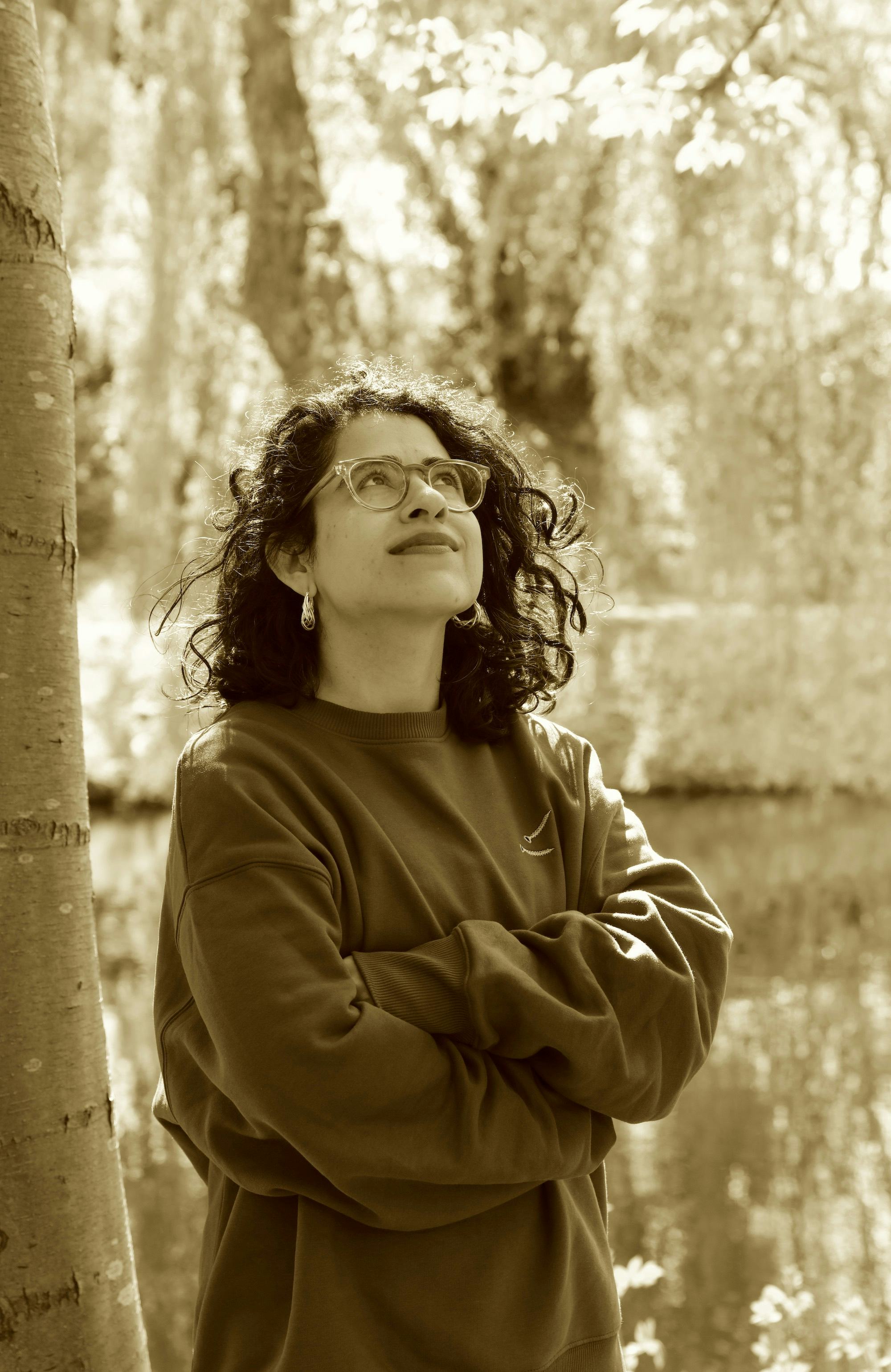 Portrait of artist Hira Nabi in a natural environment with trees, looking up to the sky