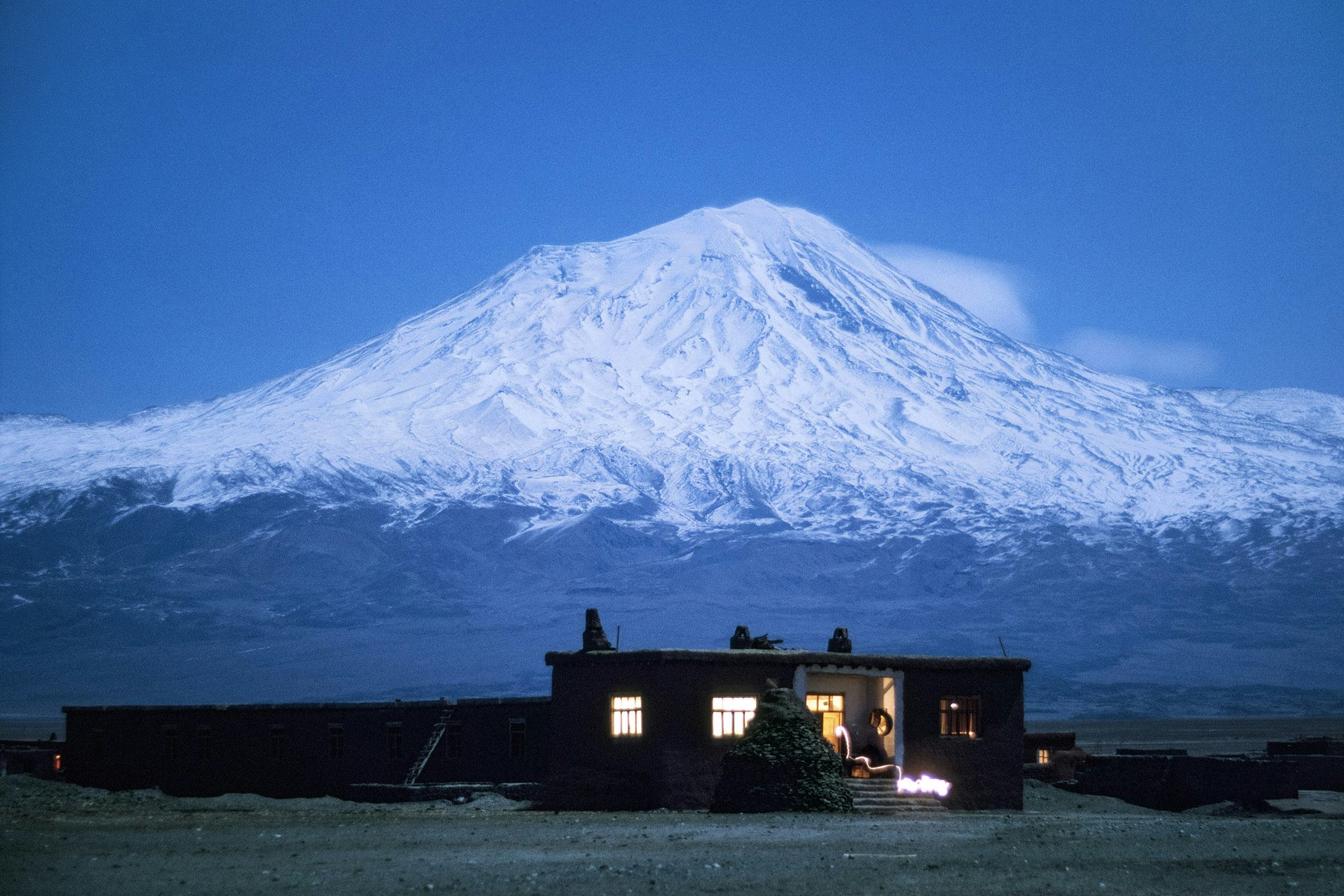 dark house with lights on and snowy mountain in the background