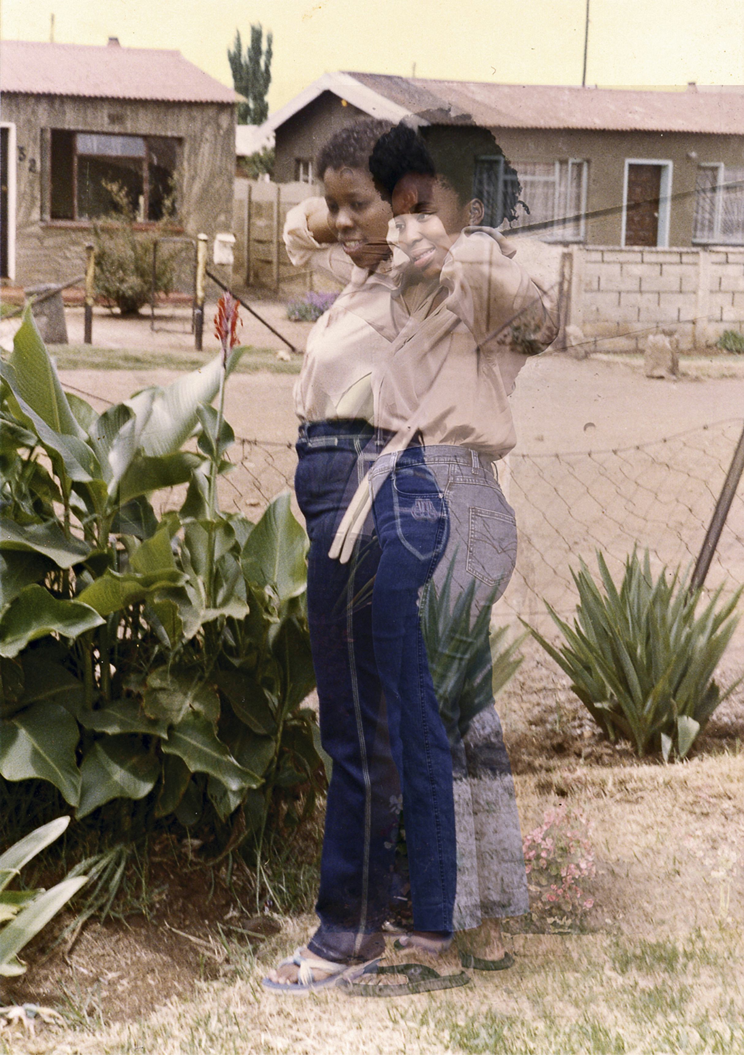 woman standing in front of house and plant wearing jeans beige blouse and slippers