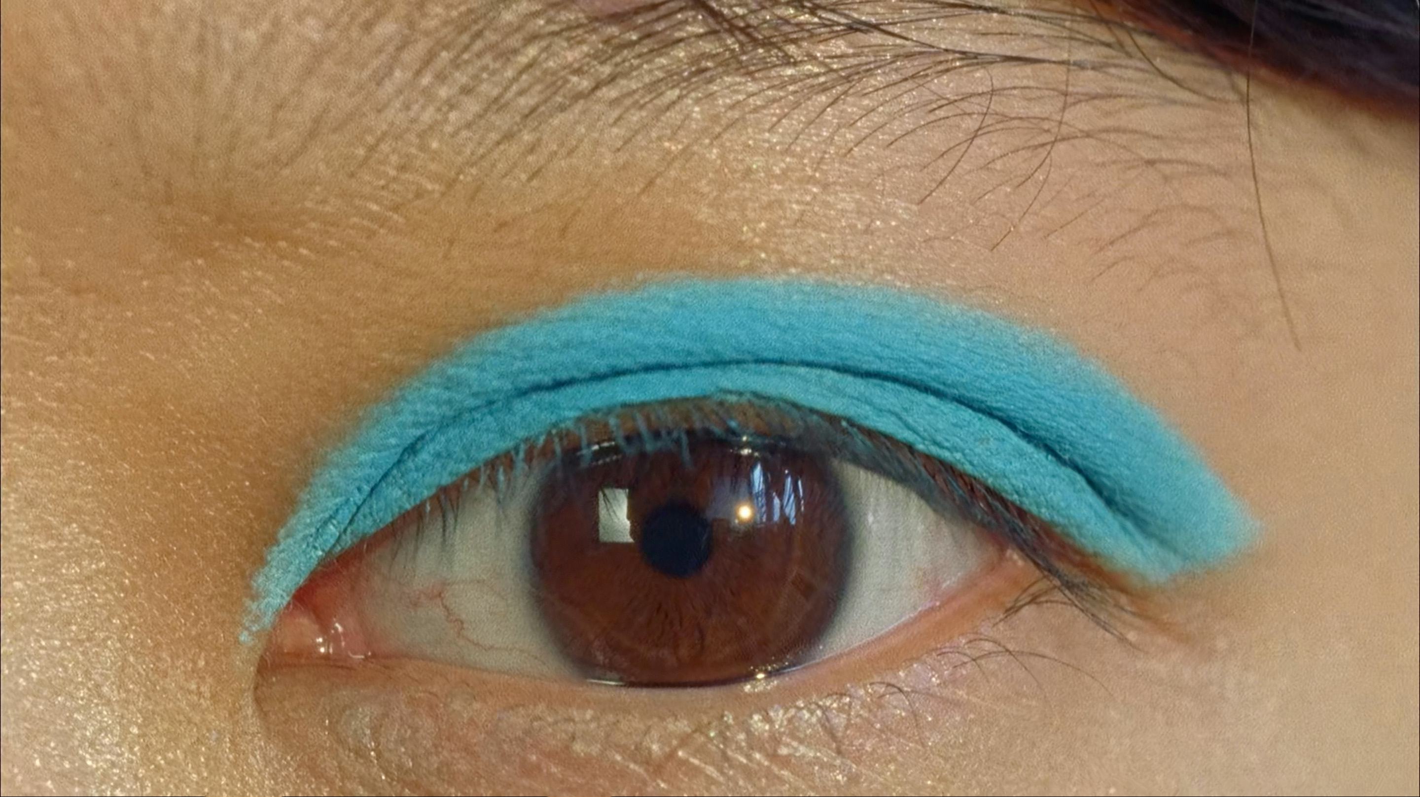 Close up of an eye with blue eyeshadow looking without emotion into the camera lense.