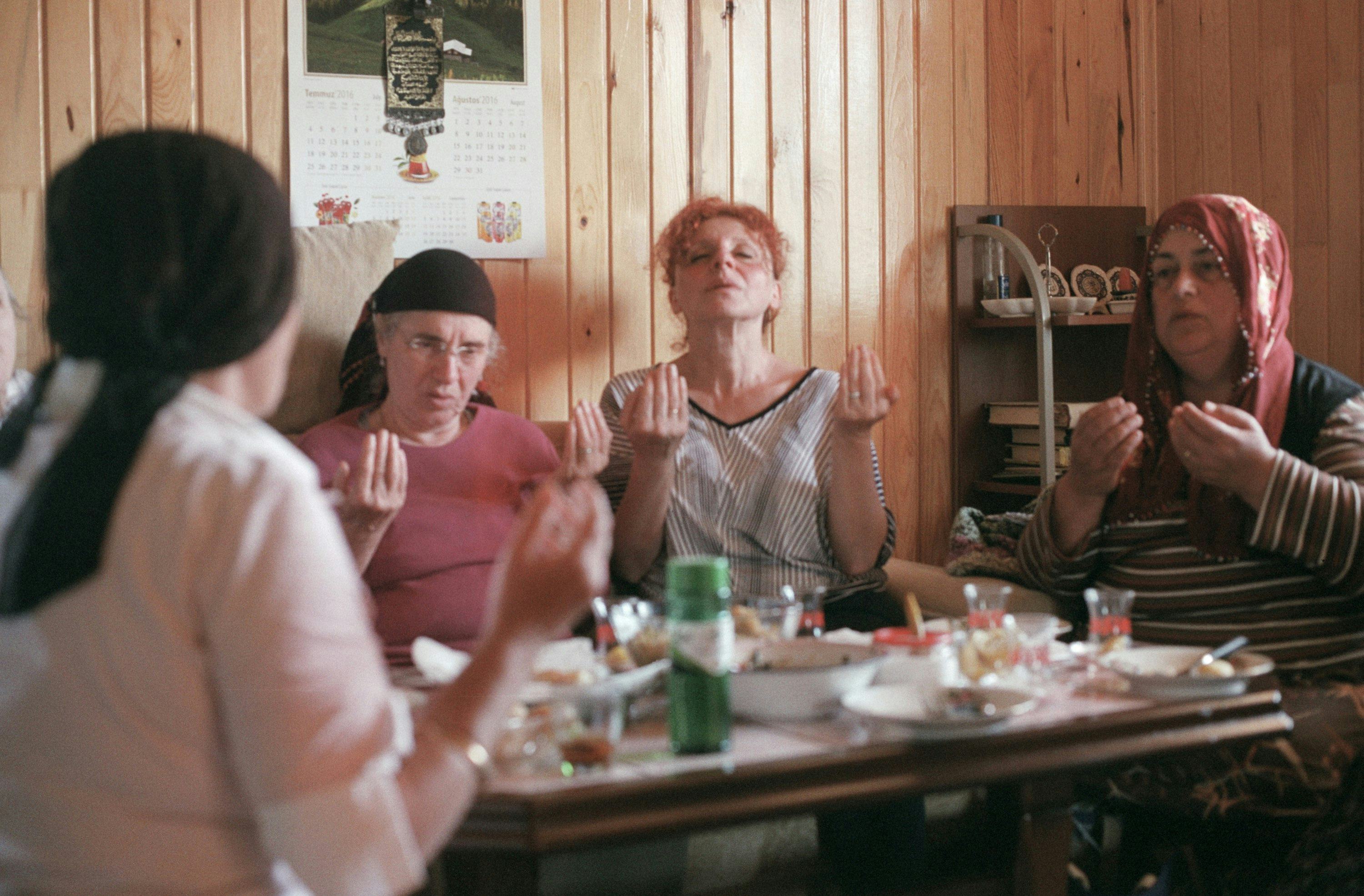 Photo of the artist's mother and other women of the family praying and enjoying a meal. © Cansu Yıldıran