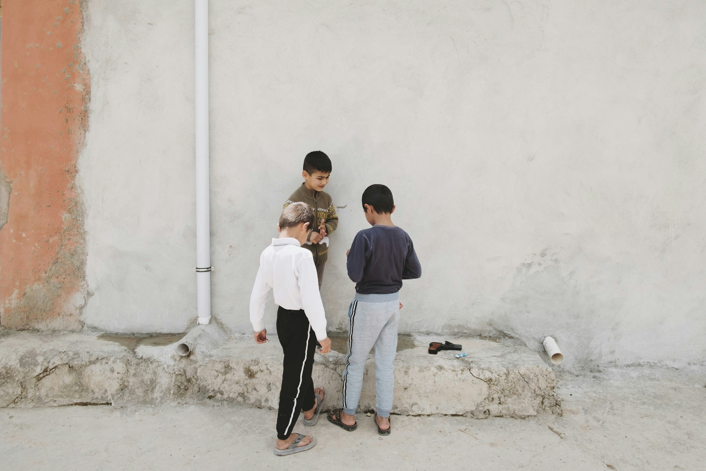 Three little boys, hanging / playing in front of a grey wall.