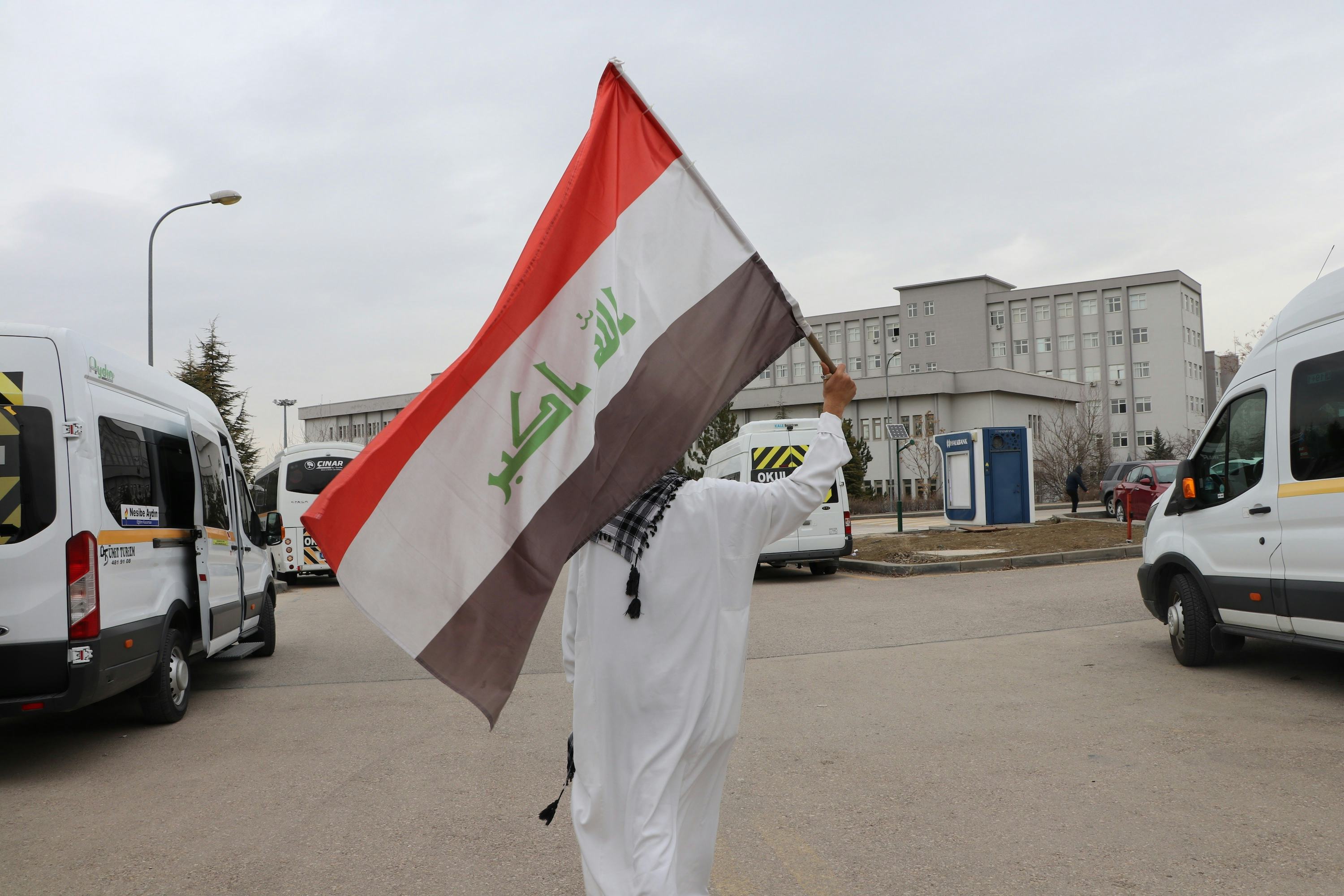 Man walking on a parking lot holding the Iraqi flag