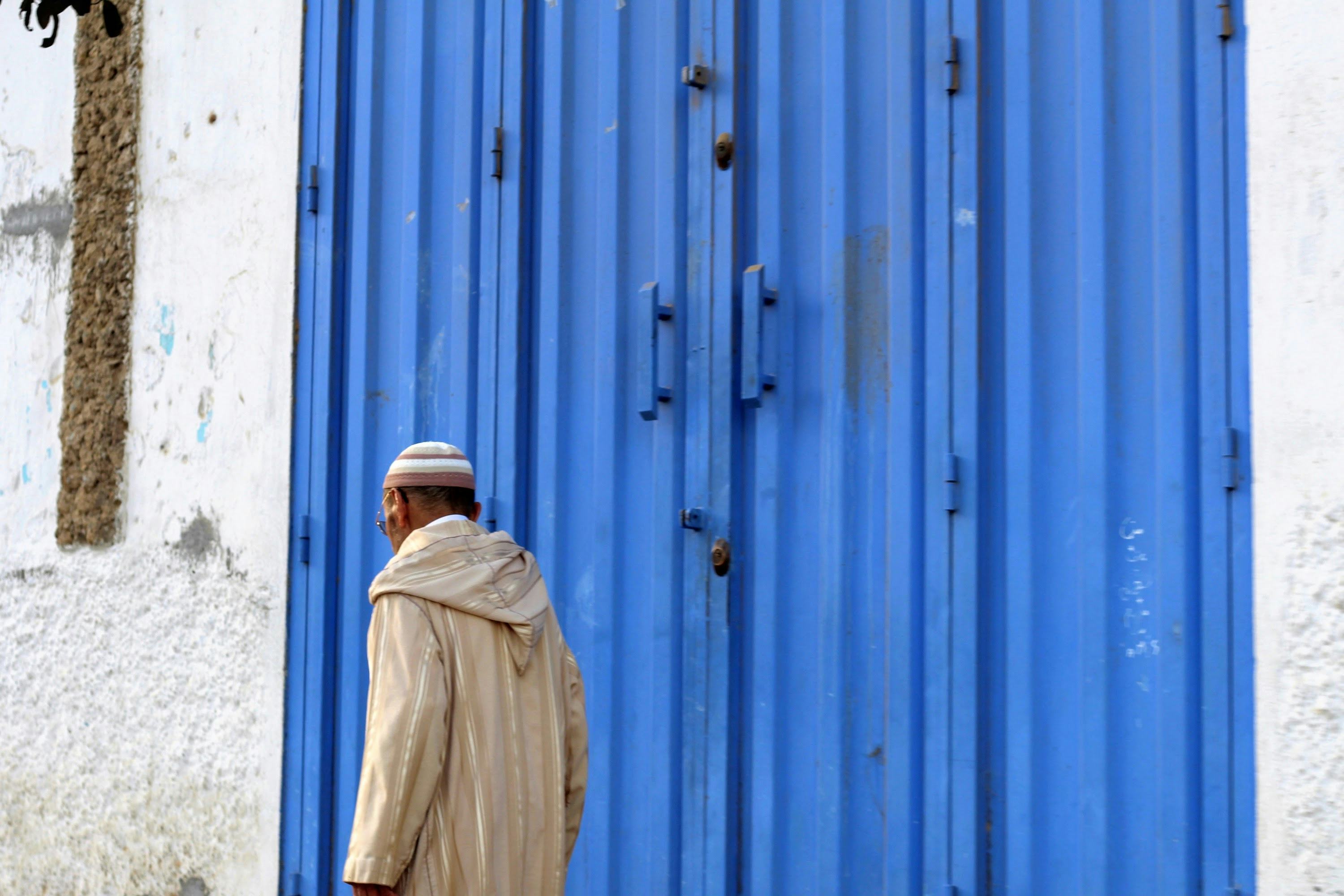 Photo of a Moroccan man passing a blue wall. © Dina Bousbaa