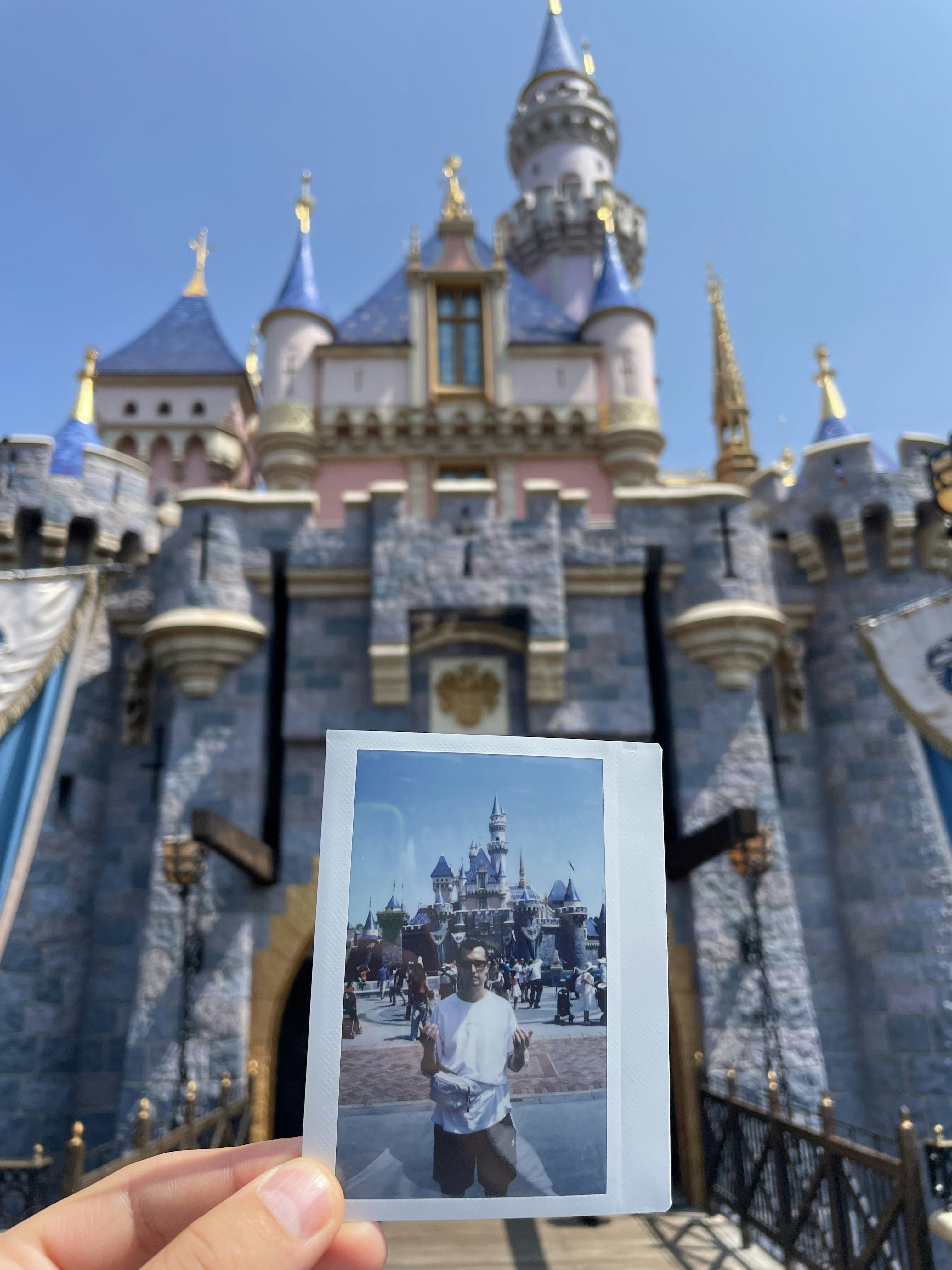 Photo of a polaroid photo in front of the Disneyland castle, showing the artist Olgac Bozalp in front of the castle.
