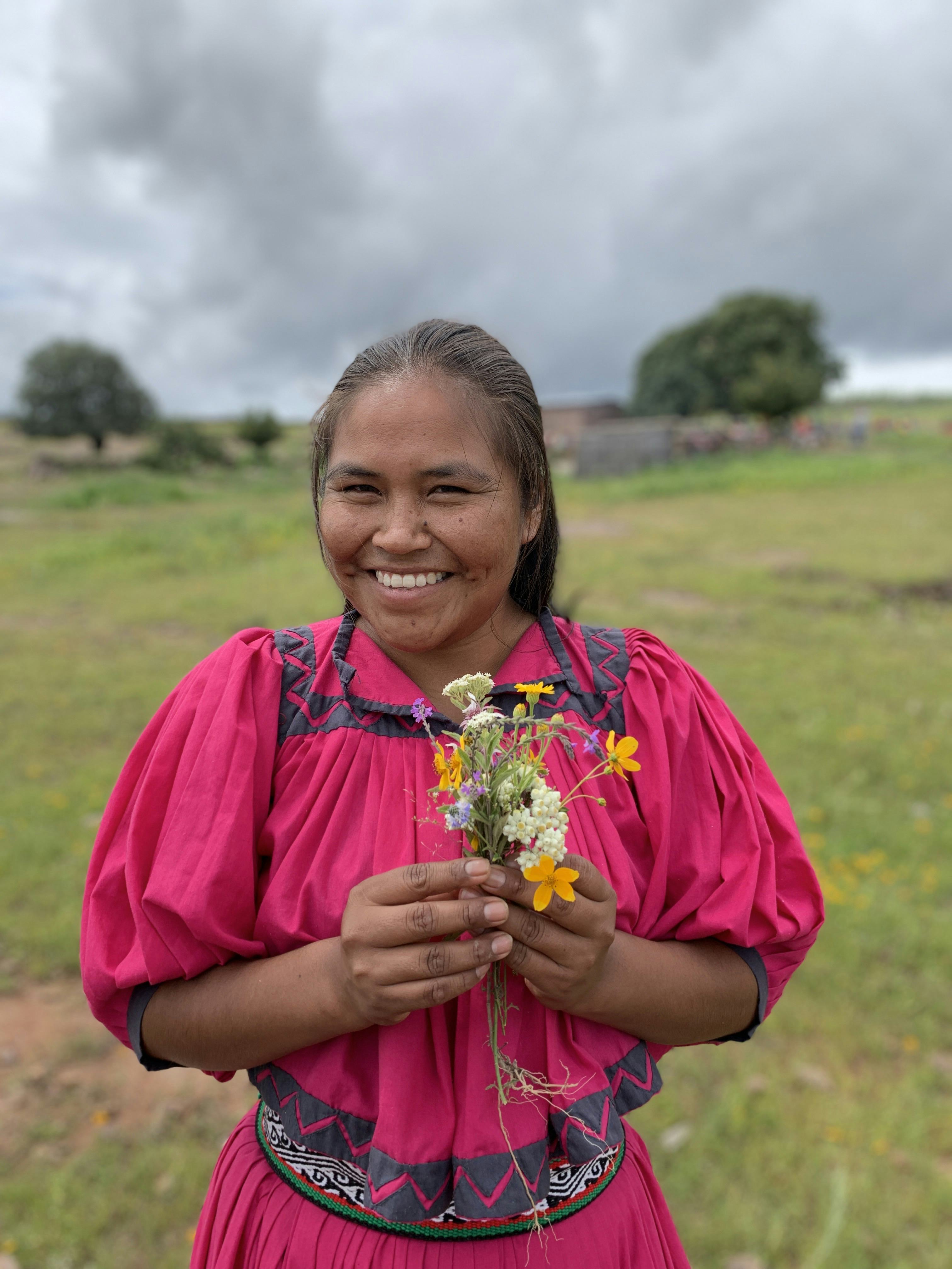 Woman in pink traditional dress holding flowers and smiling at the camera