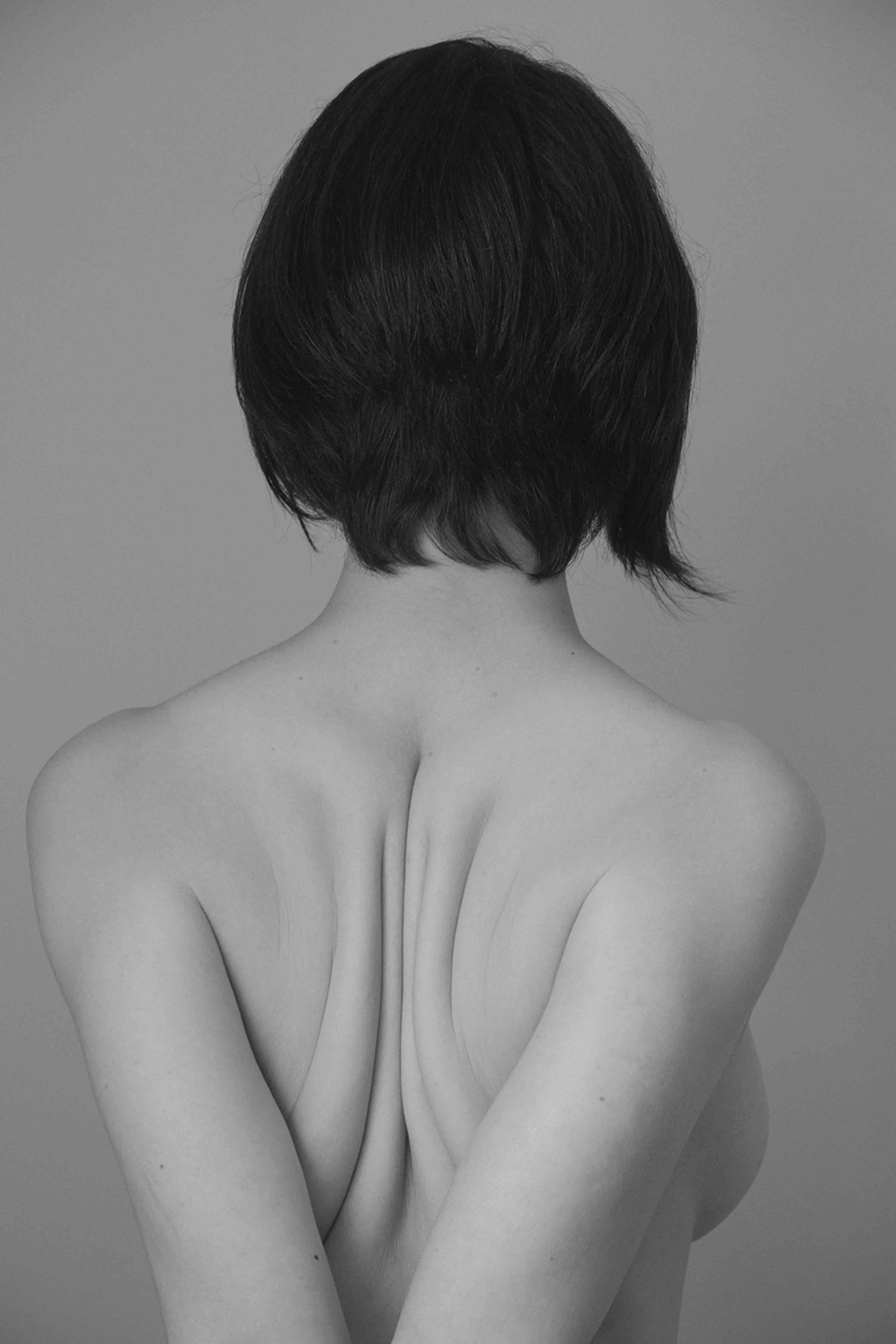 Black and white portrait of the back of a woman, with short black hair, her arms pulled backwards, pushing her shoulder blades together© Marisol Mendez