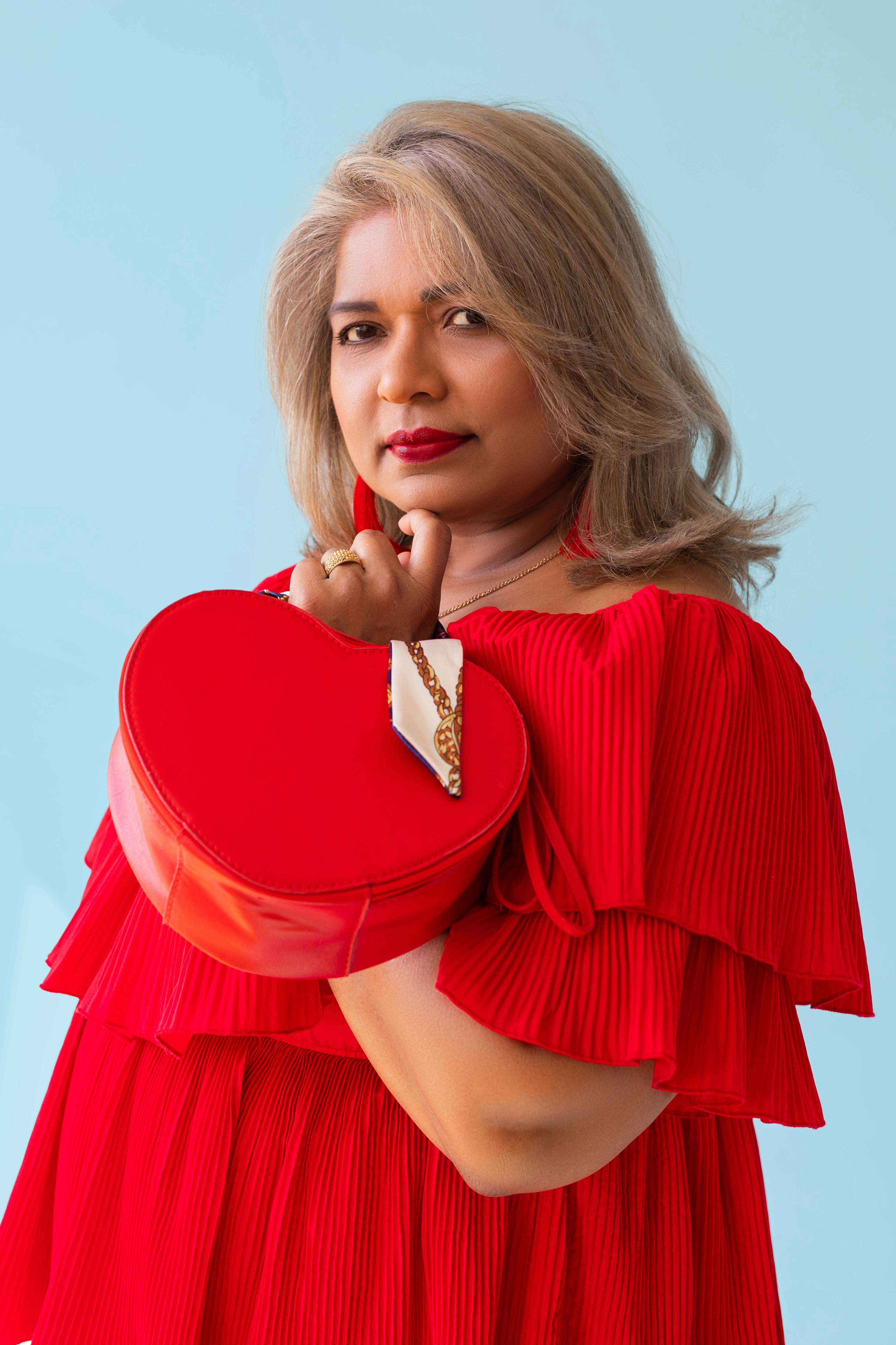 Portrait of the photographer's mother wearing a red dress and holding a red bag. © Kyara Bhiekharie