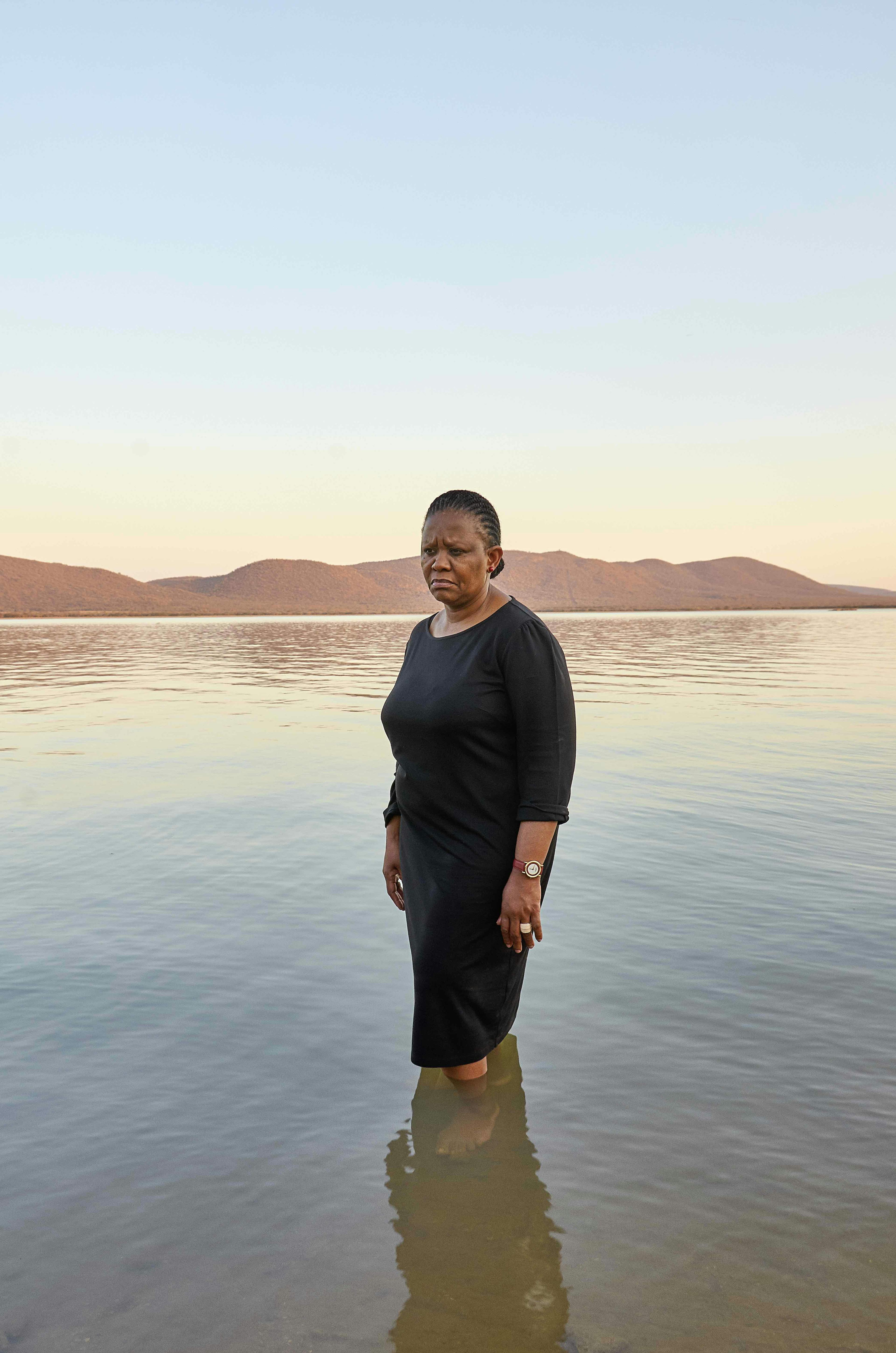 Portrait of a Black woman standing in water with mountains in the background. © Thero Makepe