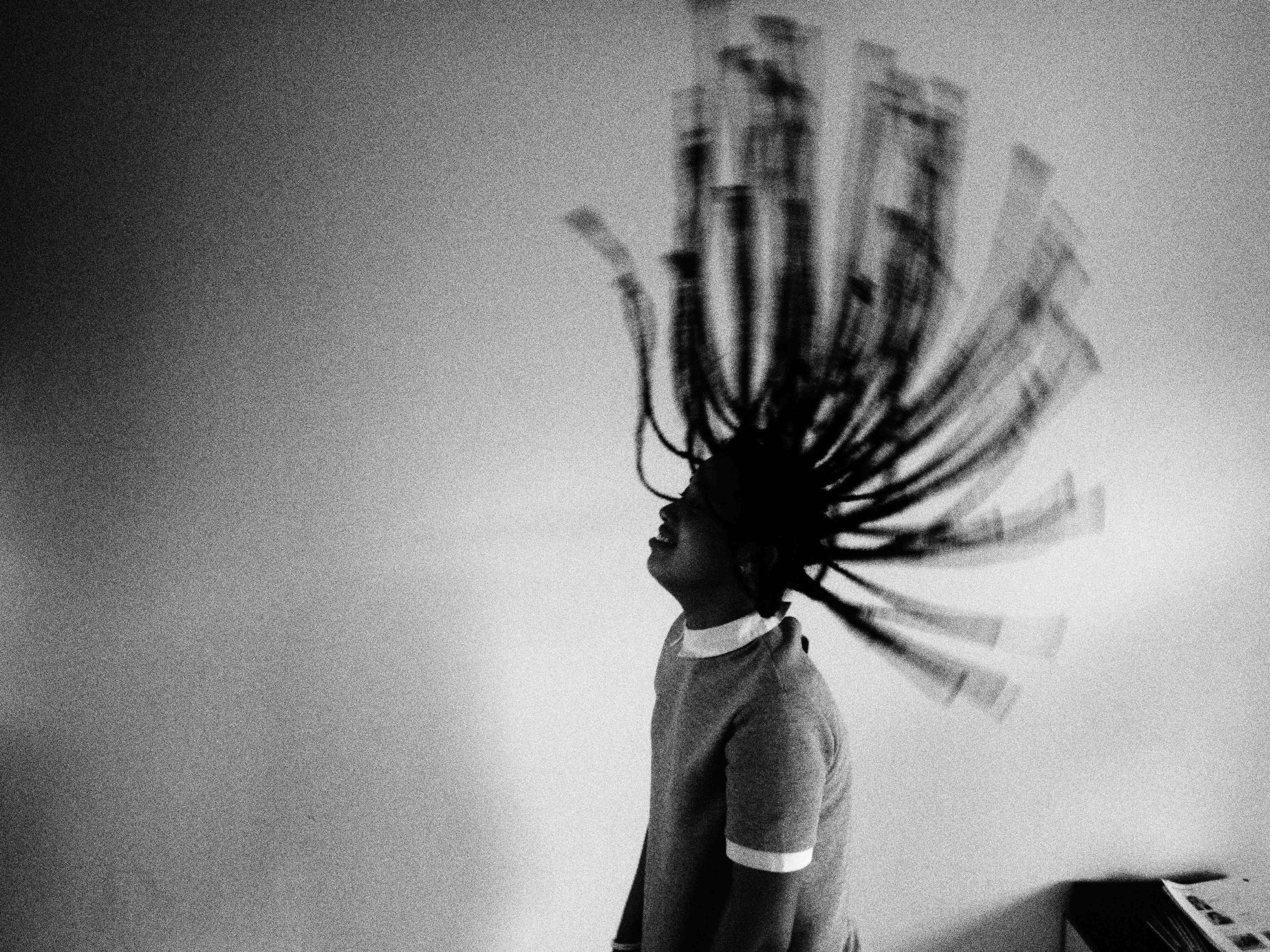 Black and white image of a girl with braids flipping her head
