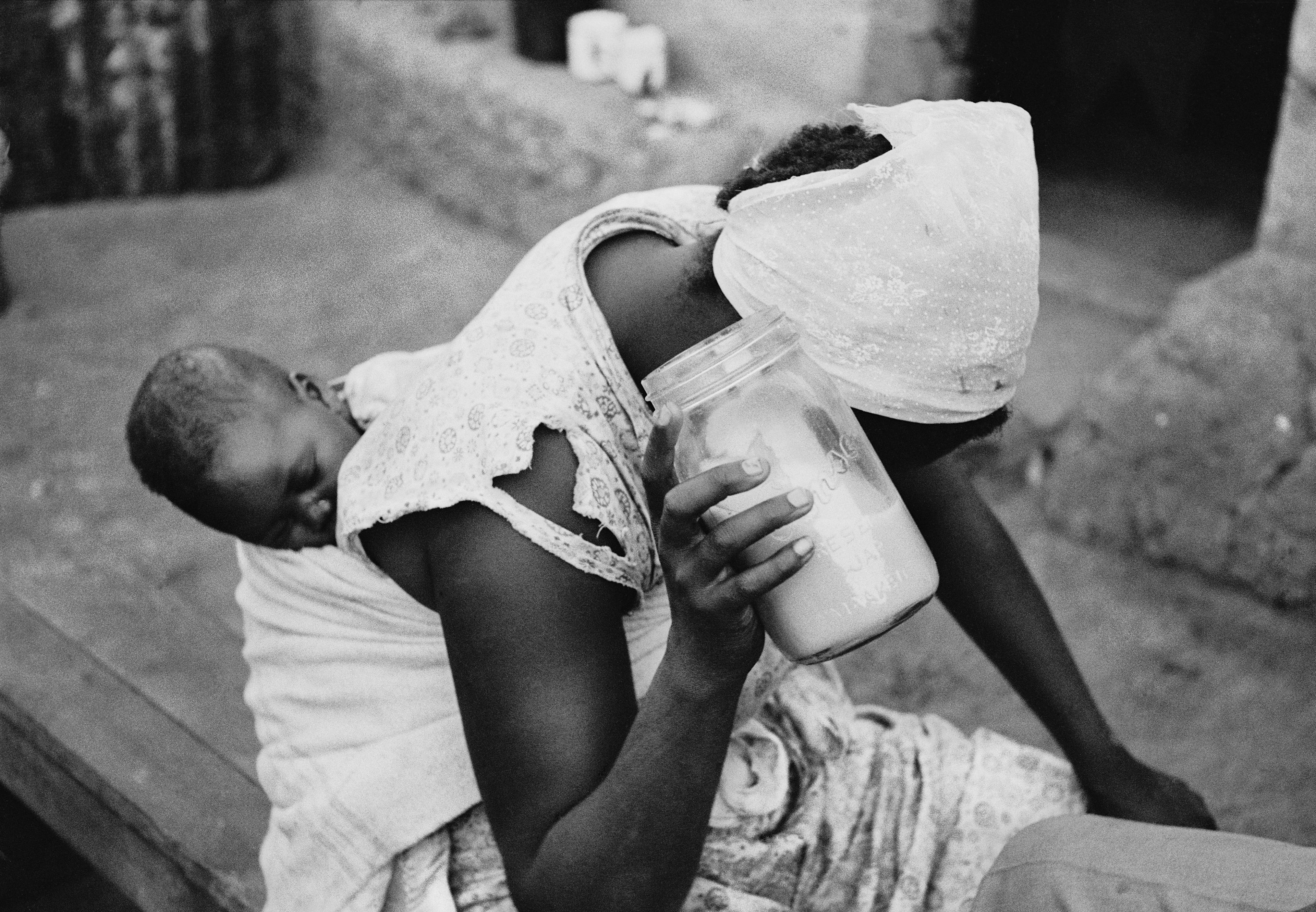 black woman holding baby on her back with milk jar