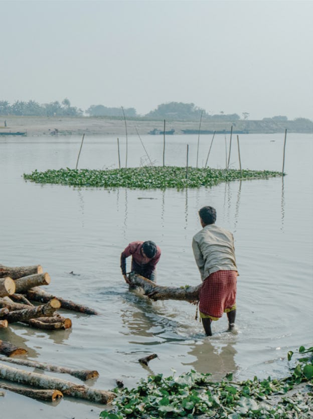 Image of two men lifting a tree out of a river in India © Akshay Mahajan
