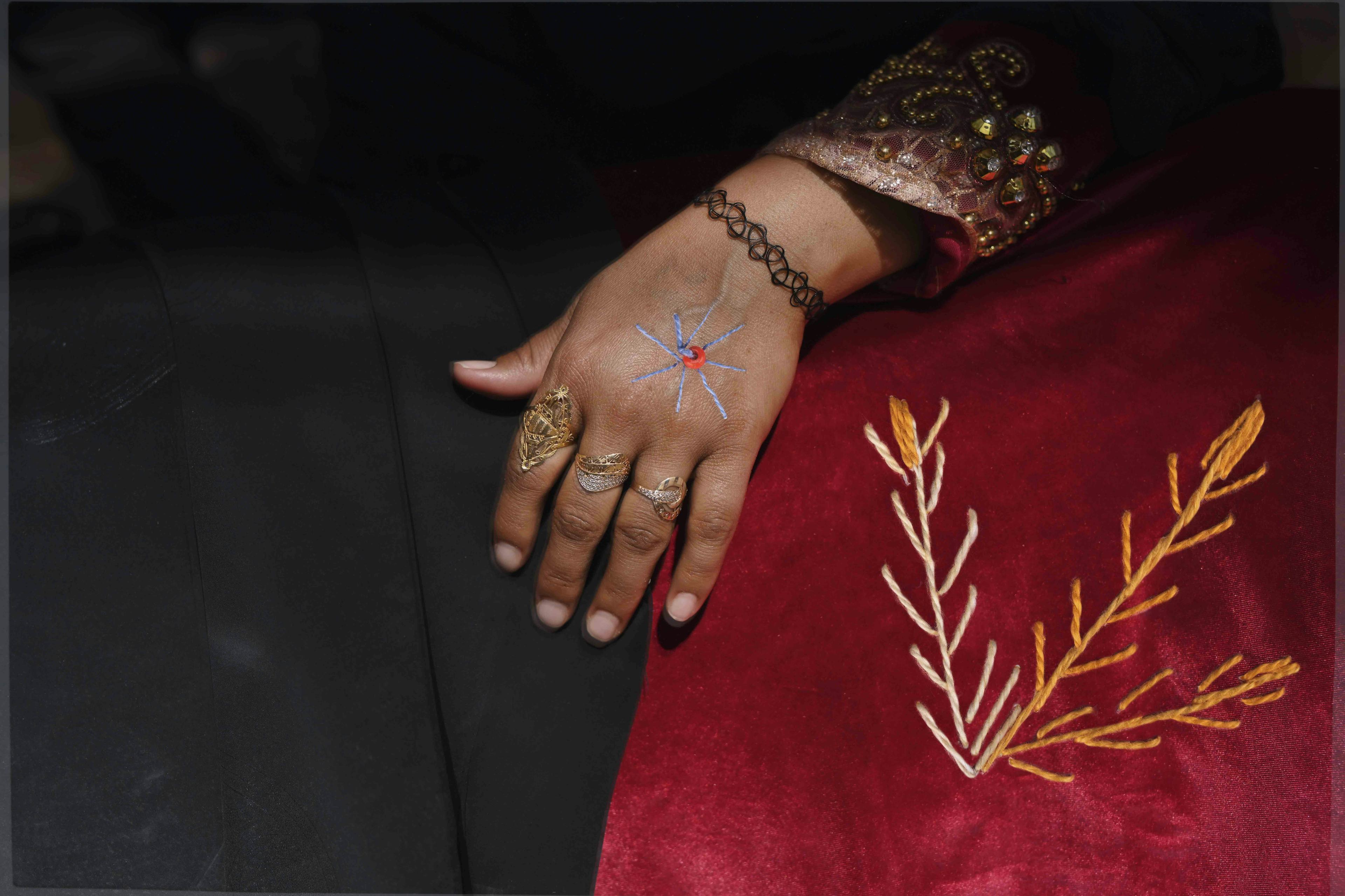 Close-up of a woman's hand, with bracelet and rings. Some geometric embroidering is covering her skirt and hand© Rehab Eldalil