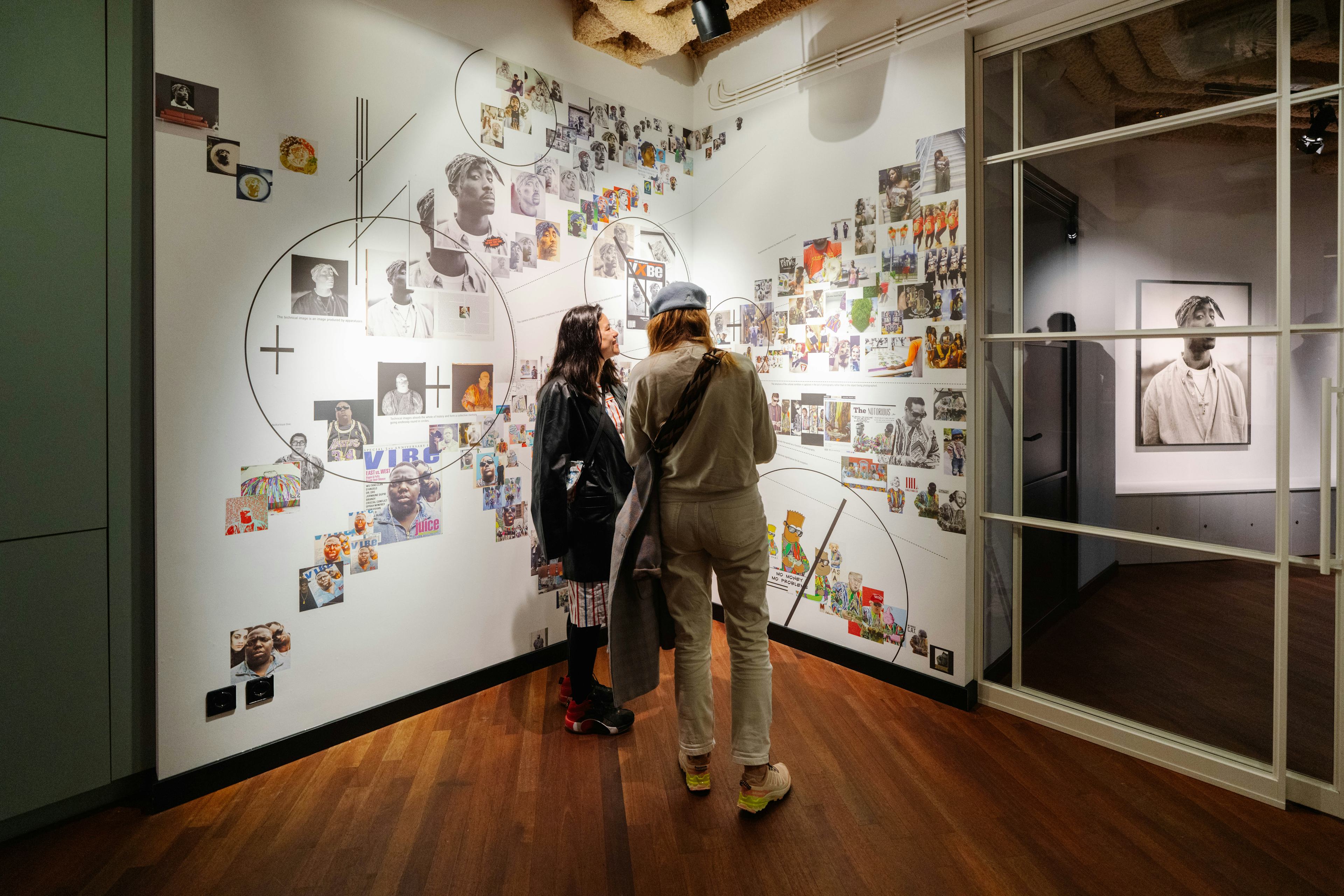 Two people looking at a collage of work in an exhibition space